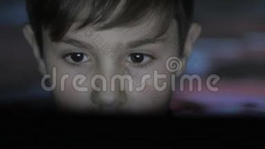 小男孩在黑暗的房间里用笔记本电脑玩电子游戏。 <strong>双倍</strong>曝光的游戏在脸上和